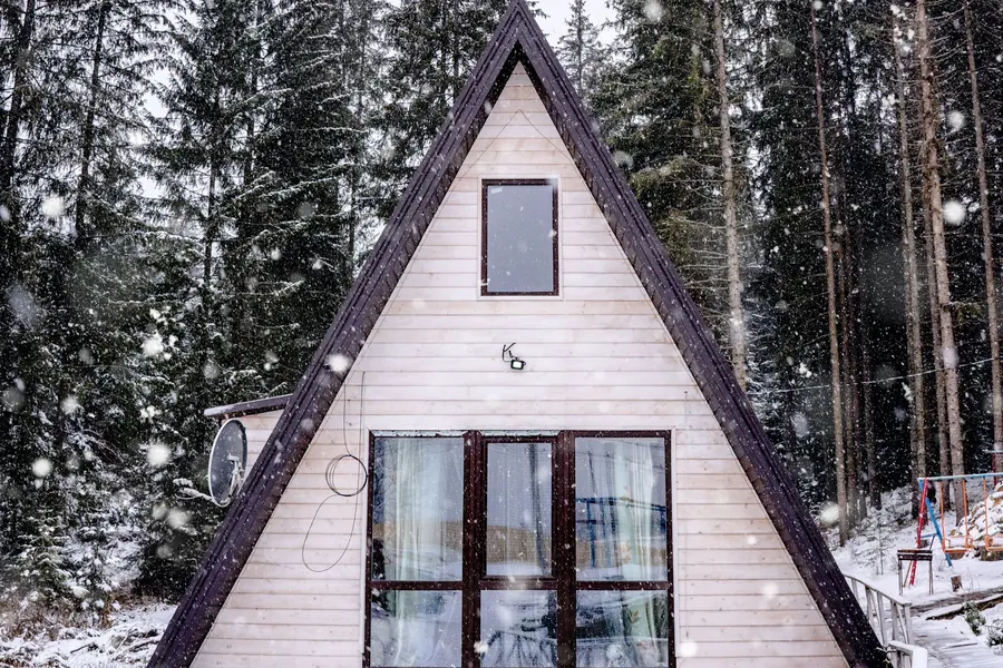 Snow-dusted A-frame cabin among pine trees